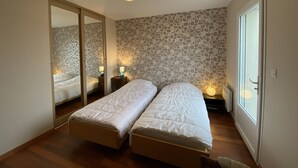 A bedroom with two single beds, a large mirror, and a stone-patterned wall. - Spacious Villa in Fouras, 10 mins from Beach, Sleeps 6, Modern Comforts, WiFi, Large Garden (Fouras)
