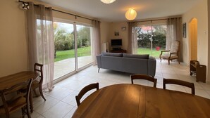 A spacious living area with a sofa, TV, and dining table. - Spacious Villa in Fouras, 10 mins from Beach, Sleeps 6, Modern Comforts, WiFi, Large Garden (Fouras)