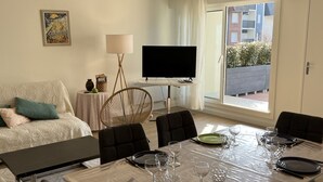 Un comedor con una mesa dispuesta para seis personas, un sofá, un televisor y una ventana con vistas a edificios.