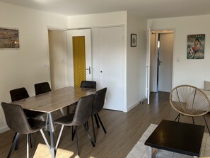 Una sala moderna con una mesa de comedor de madera, sillas negras, un sillón de mimbre y una pequeña mesa negra.
