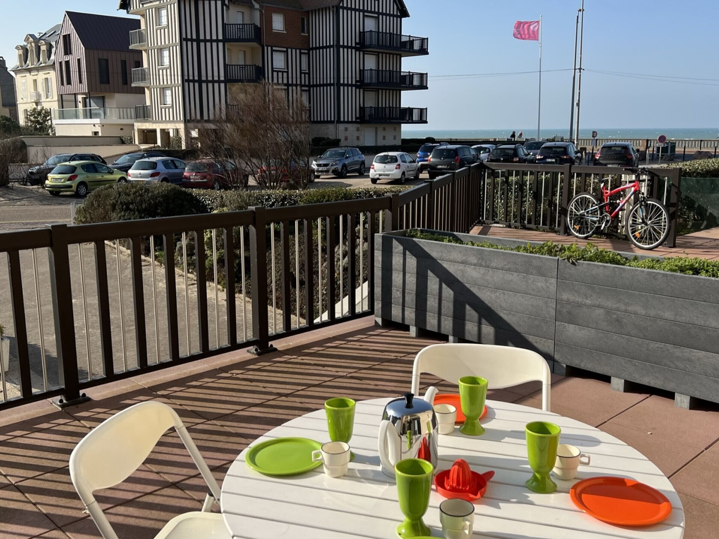 A balcony with a table set for two, overlooking a parking area and a building with a balcony.