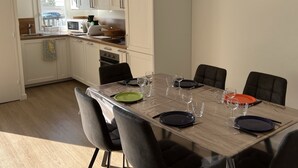 Una cocina moderna con armarios blancos, una mesa de comedor con platos y vasos, y vistas a la calle.