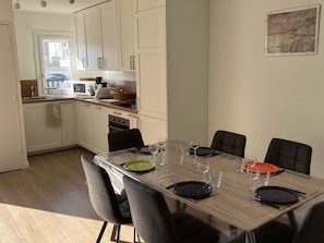 Cozinha moderna com armários brancos, mesa de jantar posta com pratos e copos, e vista para a rua.