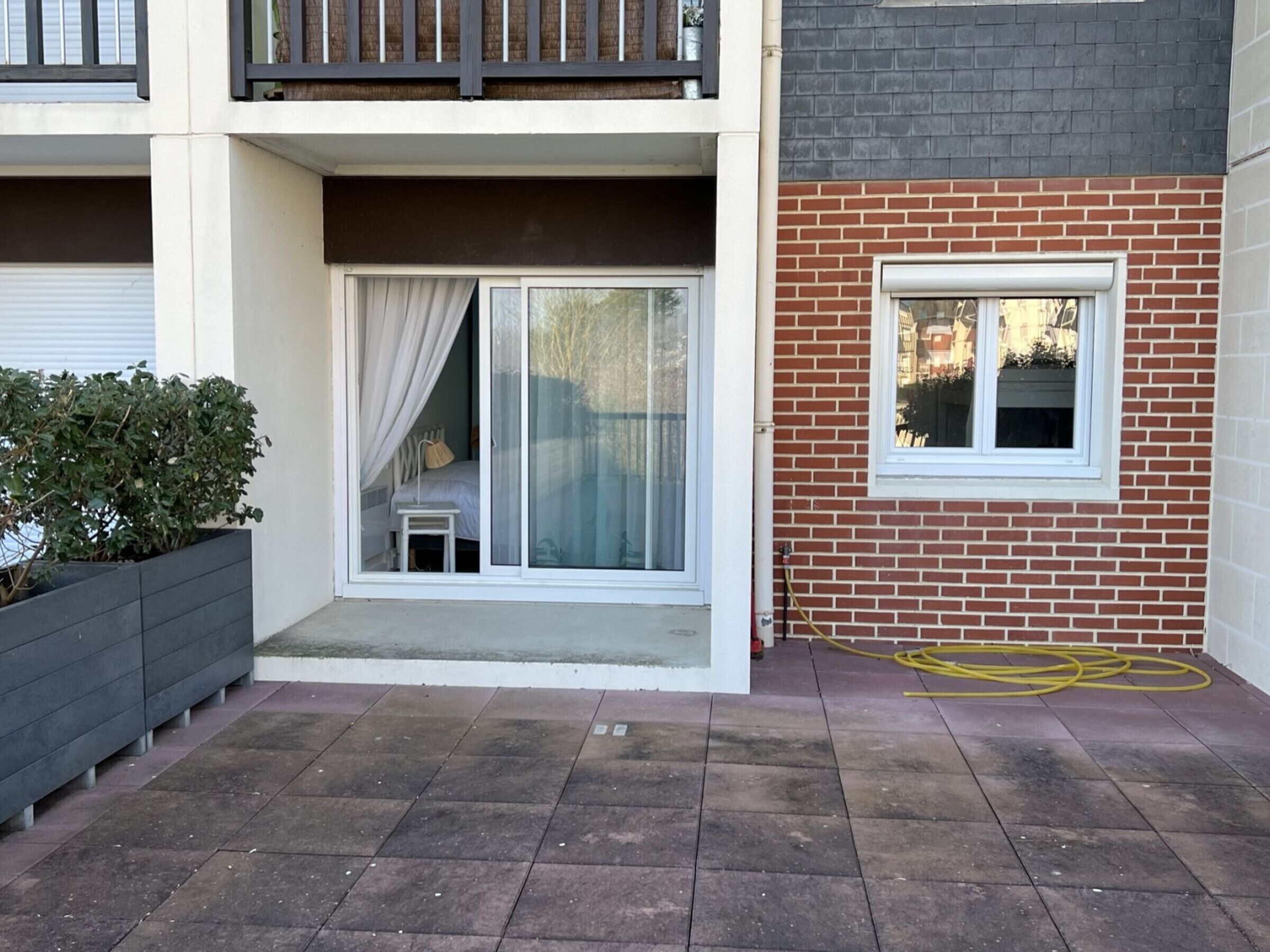 Un immeuble résidentiel doté d’un balcon, d’une porte-fenêtre coulissante donnant sur une chambre, et d’une petite fenêtre sur la façade en briques.