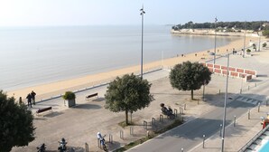 A coastal promenade with a sandy beach, a paved walkway, and a few trees. - 4-person apartment with sea view, beachfront (Fouras)