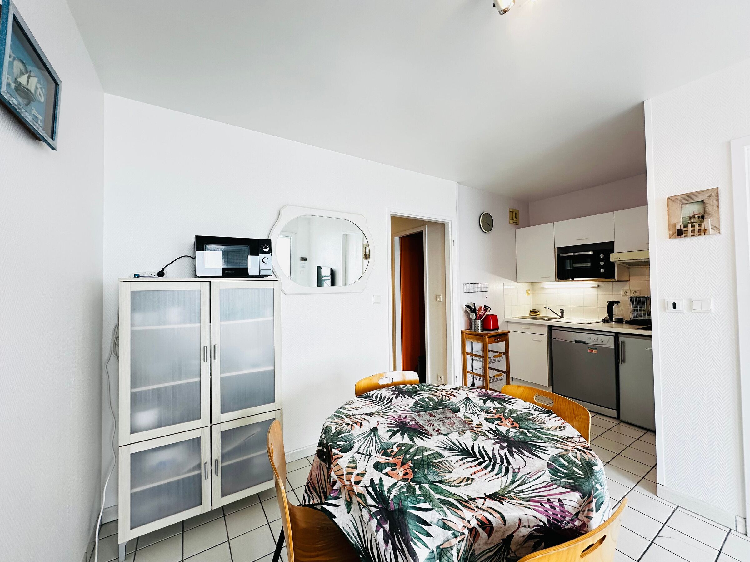 Un espace de vie compact comprenant un coin repas, une kitchenette et un mur recouvert de miroirs.