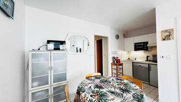 Un espace de vie compact comprenant un coin repas, une kitchenette et un mur recouvert de miroirs.