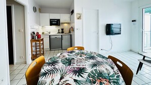 A compact kitchen with white cabinets, a microwave, and a dishwasher. There is a dining area with a table and chairs, and a TV mounted on the wall. - 4-person apartment with sea view, beachfront (Fouras)