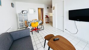 A modern living room with a grey sofa, a wooden coffee table, a TV mounted on the wall, and a dining area with a table and chairs. - 4-person apartment with sea view, beachfront (Fouras)