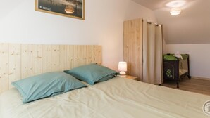 A bedroom with a wooden headboard, a bed with two pillows, a nightstand with a lamp, a window with curtains, and a small cabinet with a green top. - Cozy House near Utah Beach, Pets Allowed (Carentan les Marais-Vierville)