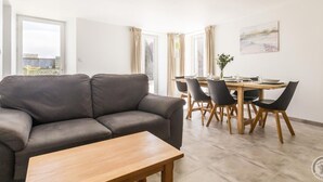 A modern living room with a grey sofa, a wooden coffee table, and a dining area with a wooden table and chairs. - Cozy House near Utah Beach, Pets Allowed (Carentan les Marais-Vierville)