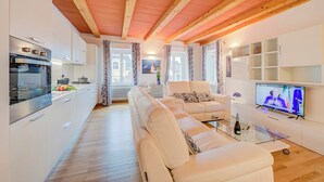 A modern living room with a sofa, a TV, and a kitchen area with an oven. - Concordia Apartment Laveno (Laveno Mombello)