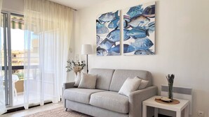 A modern living room with a grey sofa, a small white side table, and a large window with sheer curtains.