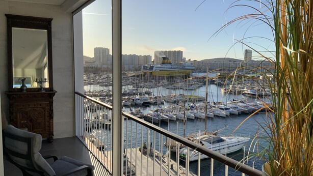 Een balkon met uitzicht op een jachthaven, een stoel, een bloempot en een spiegel.