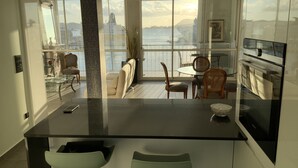 Een moderne keuken met een groot eiland, een eetgedeelte met stoelen en uitzicht op de zee.