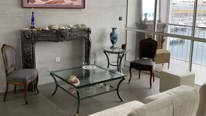 Een moderne woonkamer met een open haard, een glazen salontafel, een bank en uitzicht op de jachthaven door grote ramen.