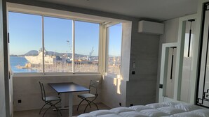 Een slaapkamer met een groot bed, een kleine tafel met twee stoelen, en een raam met uitzicht op een haven en gebouwen.