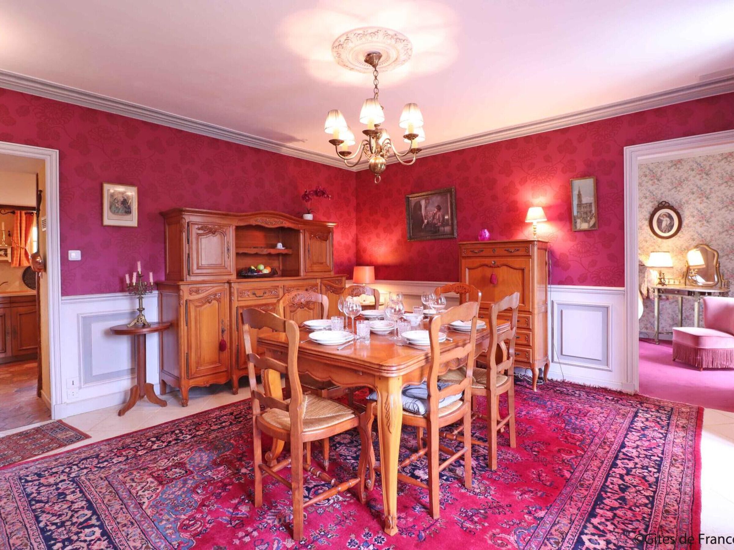 Ein Esszimmer mit einem Holztisch, gedeckt für sechs Personen, umgeben von Stühlen, einer Chandelieber und einem gemusterten Teppich.