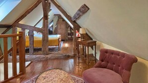 A loft bedroom with a sloped ceiling, wooden beams, a bed, a chair, and a small table. - Charming house with enclosed garden in Saint-Pierre-des-Loges (Saint-Pierre-des-Loges)