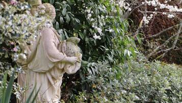 Una estatua de una figura sosteniendo una piedra, rodeada de follaje denso y plantas con flores.