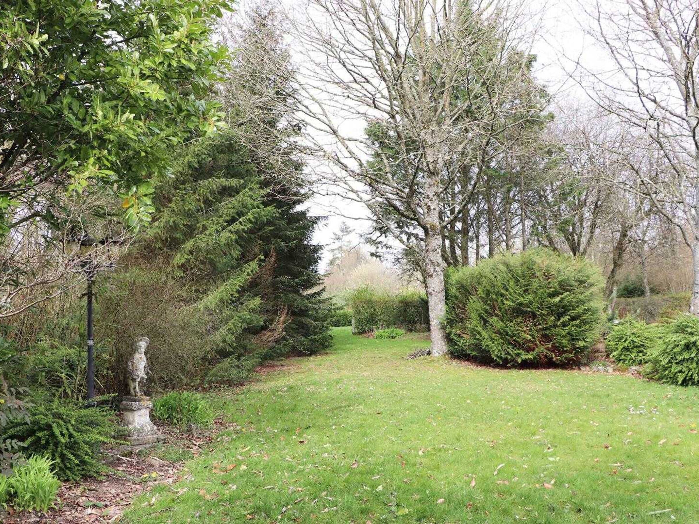 A garden with a statue, various trees, and a well-maintained lawn.