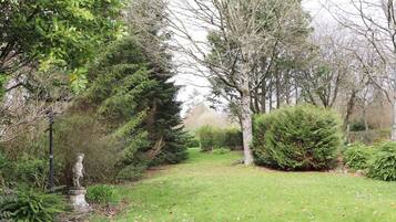 A garden with a statue, various trees, and a well-maintained lawn.