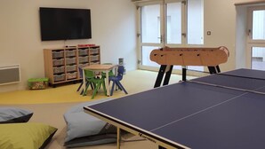 A room with a ping pong table, a television, a foosball table, and a children's play area with toys and storage bins. - Spacious Countryside Retreat with Game Room and Accessible Facilities (Loye-sur-Arnon)