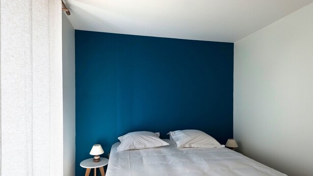 A bedroom with a single bed, white bedding, a small bedside table with a lamp, and a blue accent wall. - Spacious Countryside Retreat with Game Room and Accessible Facilities (Loye-sur-Arnon)