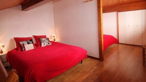 A bedroom with a wooden ceiling, a bed with red bedding, and a nightstand with a lamp. - Studio mezzanine Les Saisies - 4 pers, south balcony, station center (Les Saisies)