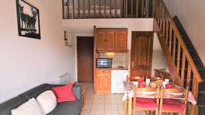 A cozy living room with a grey sofa, a dining table with chairs, a kitchen area with wooden cabinets, and a staircase. - Studio mezzanine Les Saisies - 4 pers, south balcony, station center (Les Saisies)