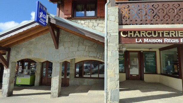 A stone building with a wooden facade, a sign for 'Charcuterie La Maison Régis', and a blue sign indicating a location. - Studio mezzanine Les Saisies - 4 pers, south balcony, station center (Les Saisies)