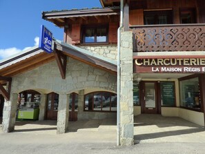 A stone building with a wooden facade, a sign for 'Charcuterie La Maison Régis', and a blue sign indicating a location. - Studio mezzanine Les Saisies - 4 pers, south balcony, station center (Les Saisies)