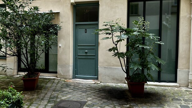 Un bâtiment avec une porte verte, des plantes en pot et une cour intérieure pavée.