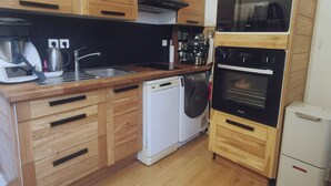 Une cuisine compacte avec des meubles en bois, un lave-linge, une machine à café et un four encastré.