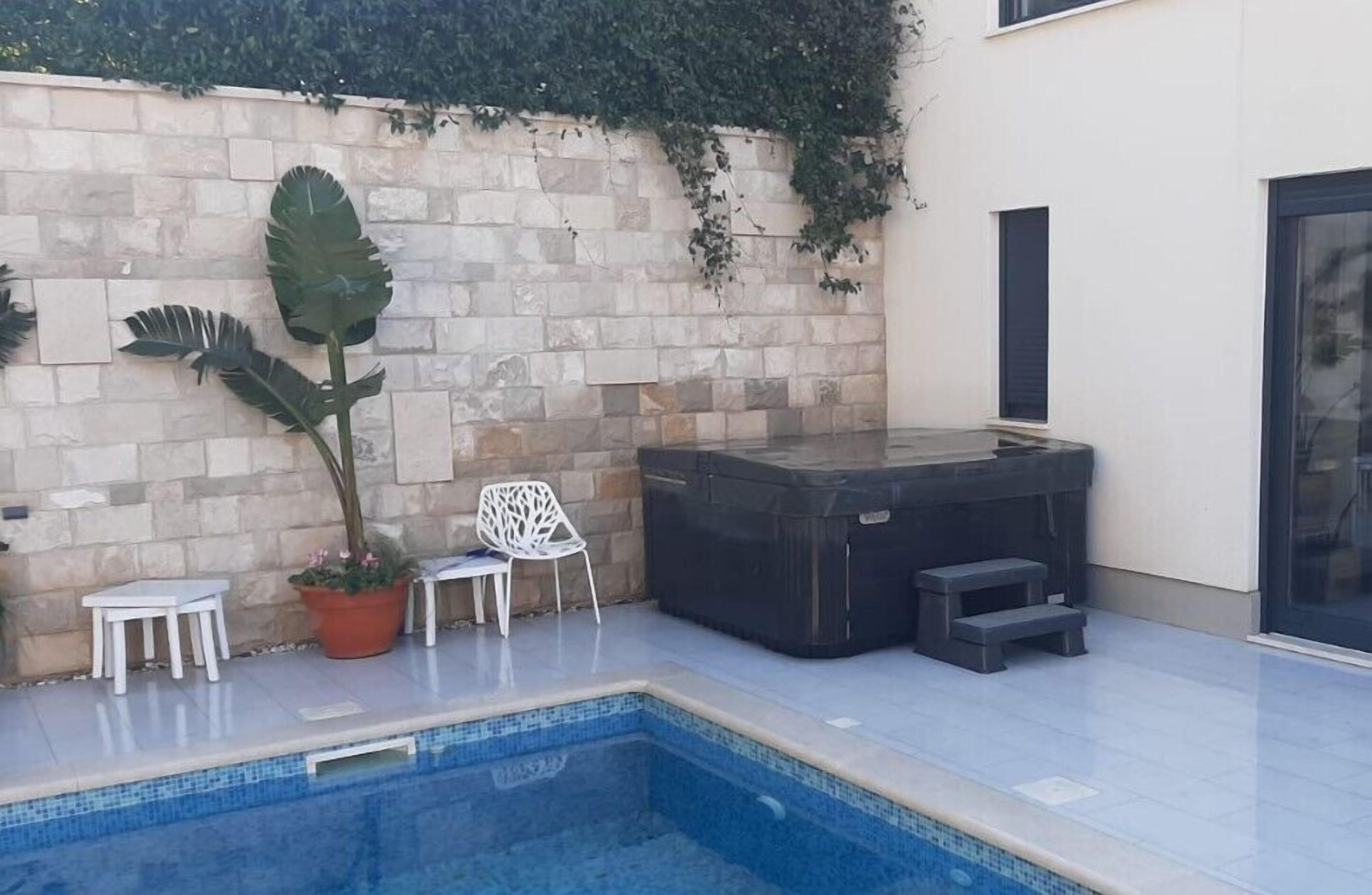 A swimming pool with a stone wall, a hot tub, and outdoor furniture.