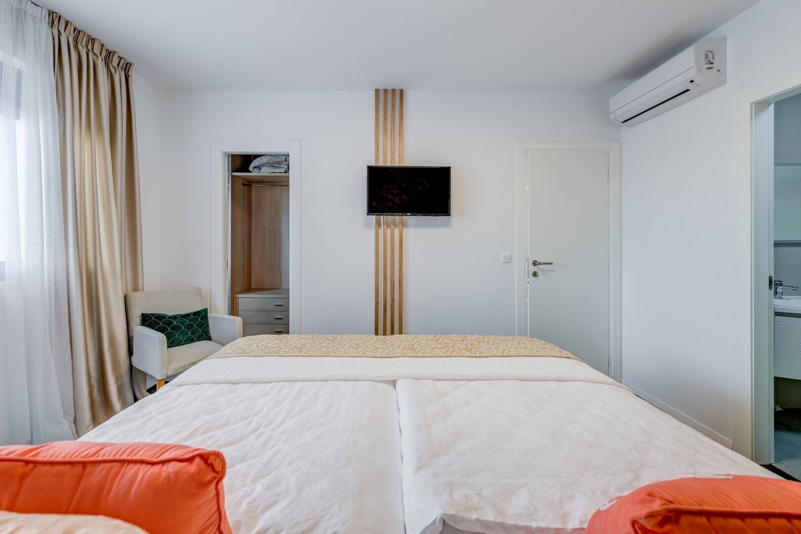 Een hotelkamer met een bed, een televisie, een airconditioning en een badkamer, zichtbaar door een geopende deur.