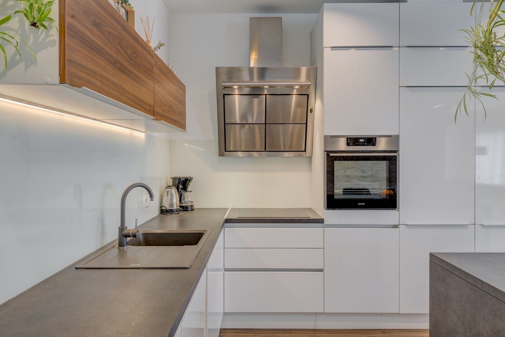 Une cuisine moderne dotée d’appareils électroménagers en acier inoxydable, de meubles blancs et d’un four encastré.