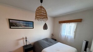 Um quarto com cama, mesa de cabeceira, abajur, luminária pendente, janela com cortinas e um quadro na parede.
