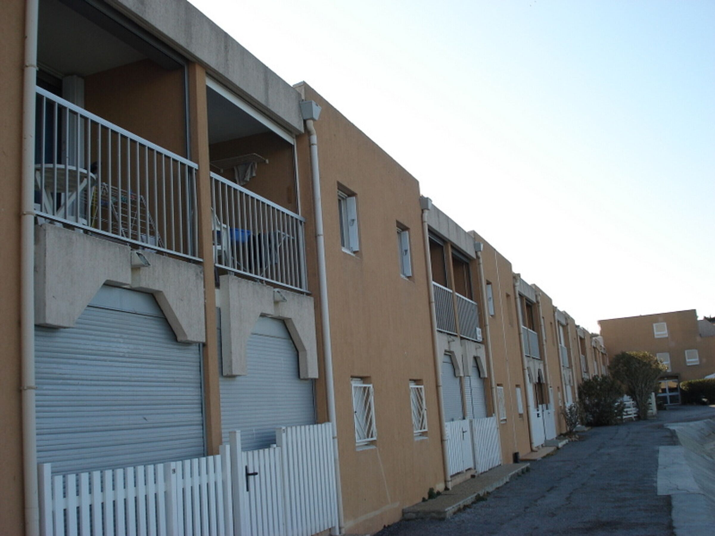 A row of residential buildings with balconies, a white picket fence, and closed shutters.