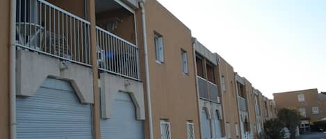 A row of residential buildings with balconies, a white picket fence, and closed shutters.