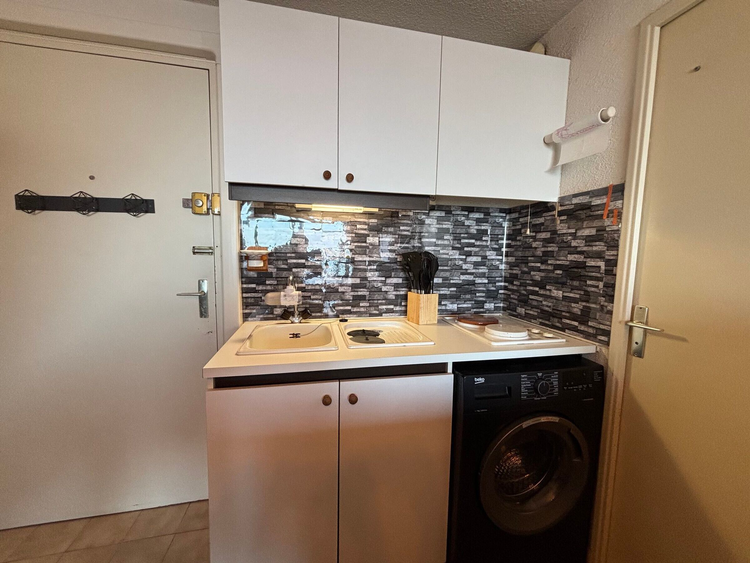 Une cuisine compacte équipée d’un lave-linge, d’un évier et d’un plan de travail avec un porte-couteaux.