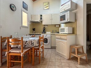 A compact kitchen with a washing machine, microwave, and a dining area with a table and chairs. - Townhouse in La Palmyre, 5 people (La Palmyre)