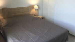 A single bed with a wooden headboard, a bedside table with a lamp, and a plain wall with a small picture frame. - Stylish 2-Story Villa with Pool, Near Beach, Sleeps 6, Parking, A/C (Cap d'Agde)