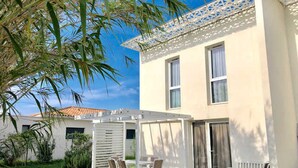 A two-story building with a covered patio area, a white exterior, and a tiled roof. - Stylish 2-Story Villa with Pool, Near Beach, Sleeps 6, Parking, A/C (Cap d'Agde)