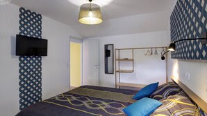 A bedroom with a bed, a hanging light fixture, a TV mounted on the wall, and a patterned wall design. - Comfortable cottage with private garden in Balbigny (Balbigny)
