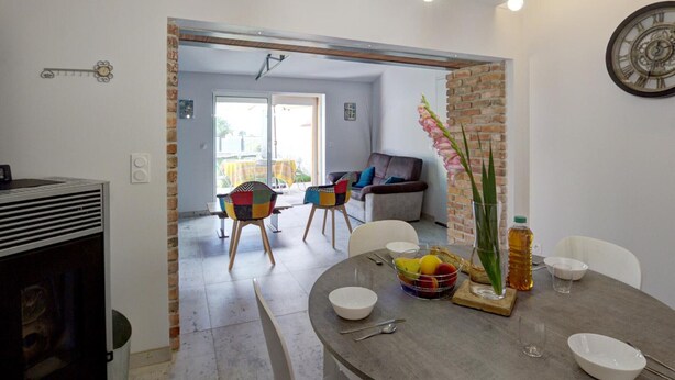 A dining area with a round table, chairs, and a vase with flowers. There is a brick wall and a clock on the wall. - Comfortable cottage with private garden in Balbigny (Balbigny)