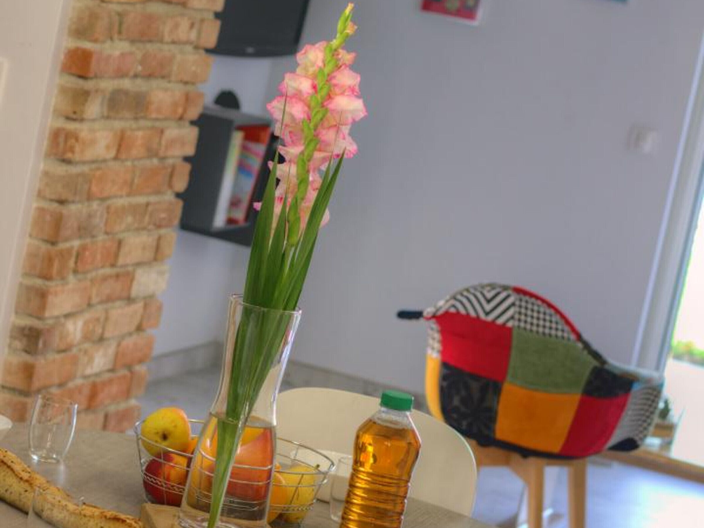 A dining table with a vase of flowers, a fruit basket, and a bottle of water.