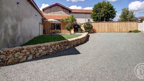 A two-story house with a stone wall, a covered patio with outdoor furniture, and a fenced yard. - Comfortable cottage with private garden in Balbigny (Balbigny)