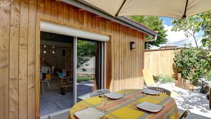 An outdoor patio with a table set for dining, wooden walls, and a sliding glass door leading to an interior space. - Comfortable cottage with private garden in Balbigny (Balbigny)