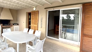 Um pátio com mesa e cadeiras brancas, lareira de tijolos e porta de vidro deslizante que dá para uma área externa coberta.